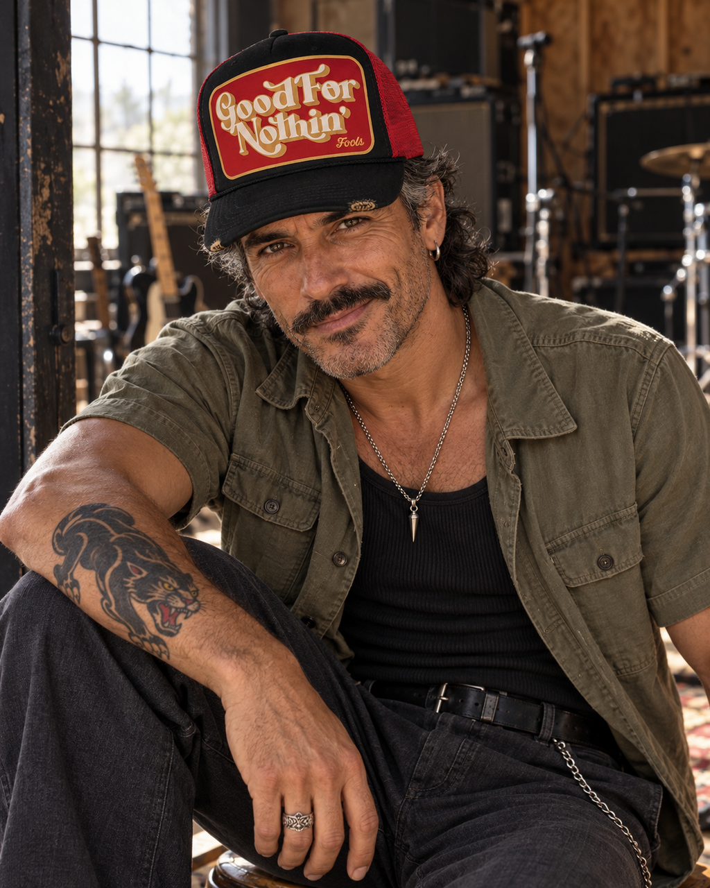 FOOLS Good For Nothin black and red trucker hat styled with an olive military work shirt, black tank and silver wallet chain in a music studio.