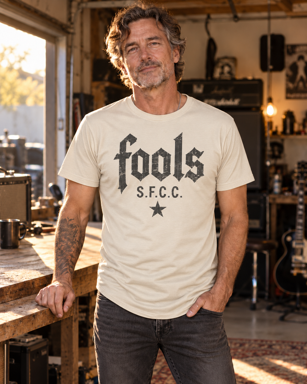 Model concept showing the FOOLS men's Ecru curved-hem tee with distressed faded-charcoal S.F.C.C. lettering and star artwork.