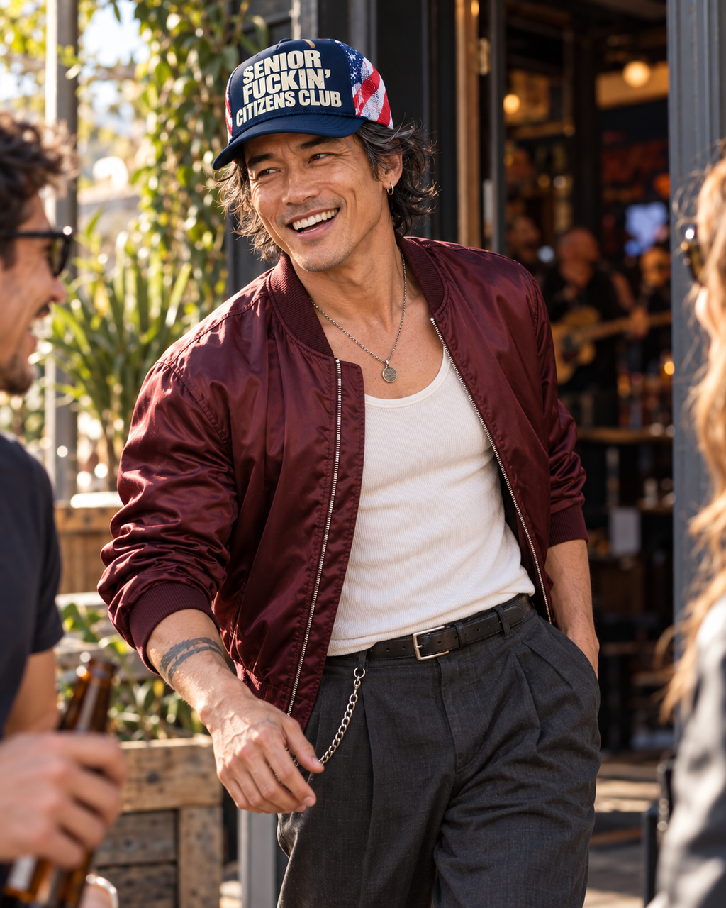 FOOLS navy trucker hat with striped mesh and cream lettering, worn with a burgundy satin bomber and charcoal trousers outside a pub
