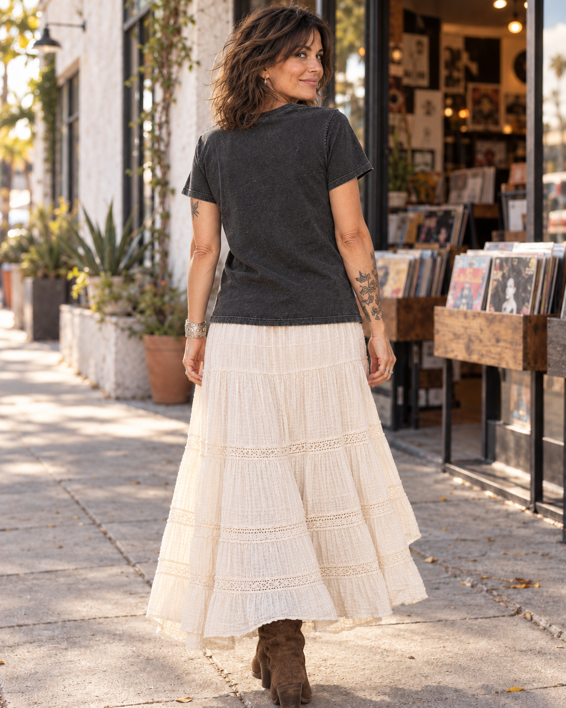 Back view of the FOOLS Women's Faded We Ain't Dead Yet Tee in faded black, showing the plain back and untucked hem with an ivory skirt