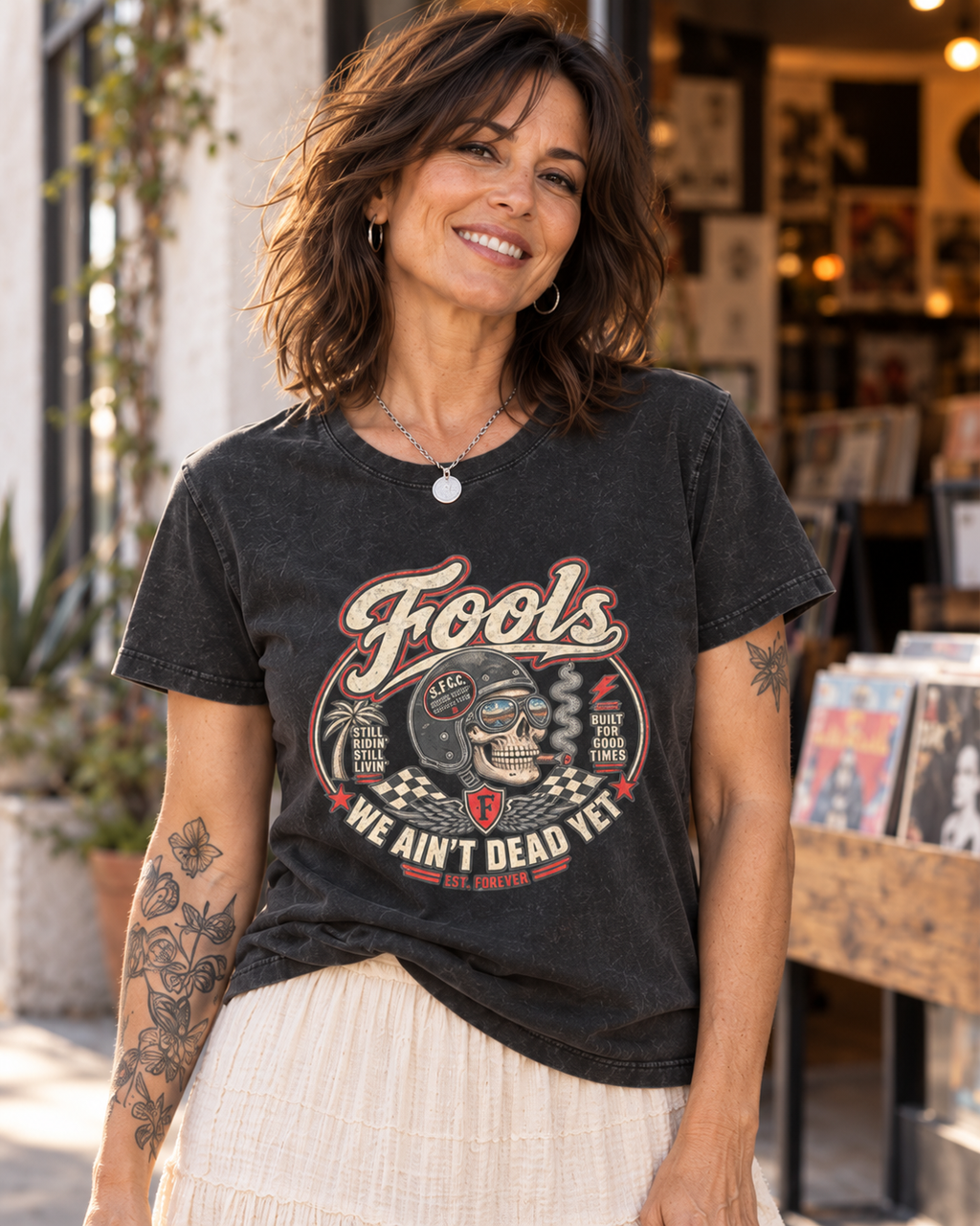 Close-up of the FOOLS Women's Faded We Ain't Dead Yet Tee in faded black, showing the distressed chest graphic with the brunette model and ivory skirt