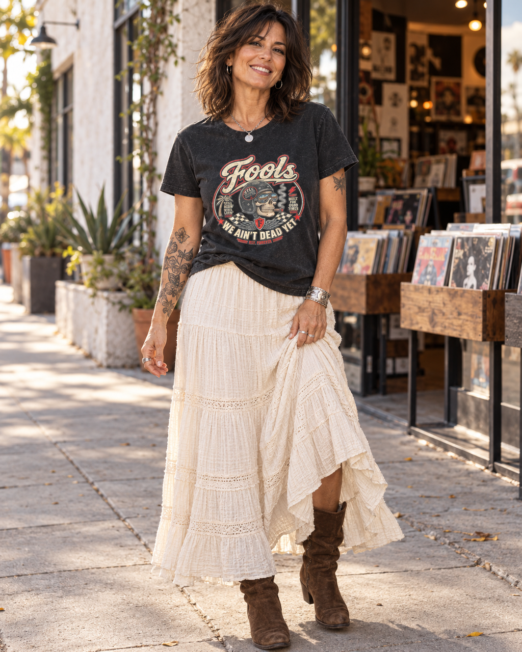 FOOLS Women's Faded We Ain't Dead Yet Tee in faded black, styled with an ivory skirt and brown boots outside a record shop