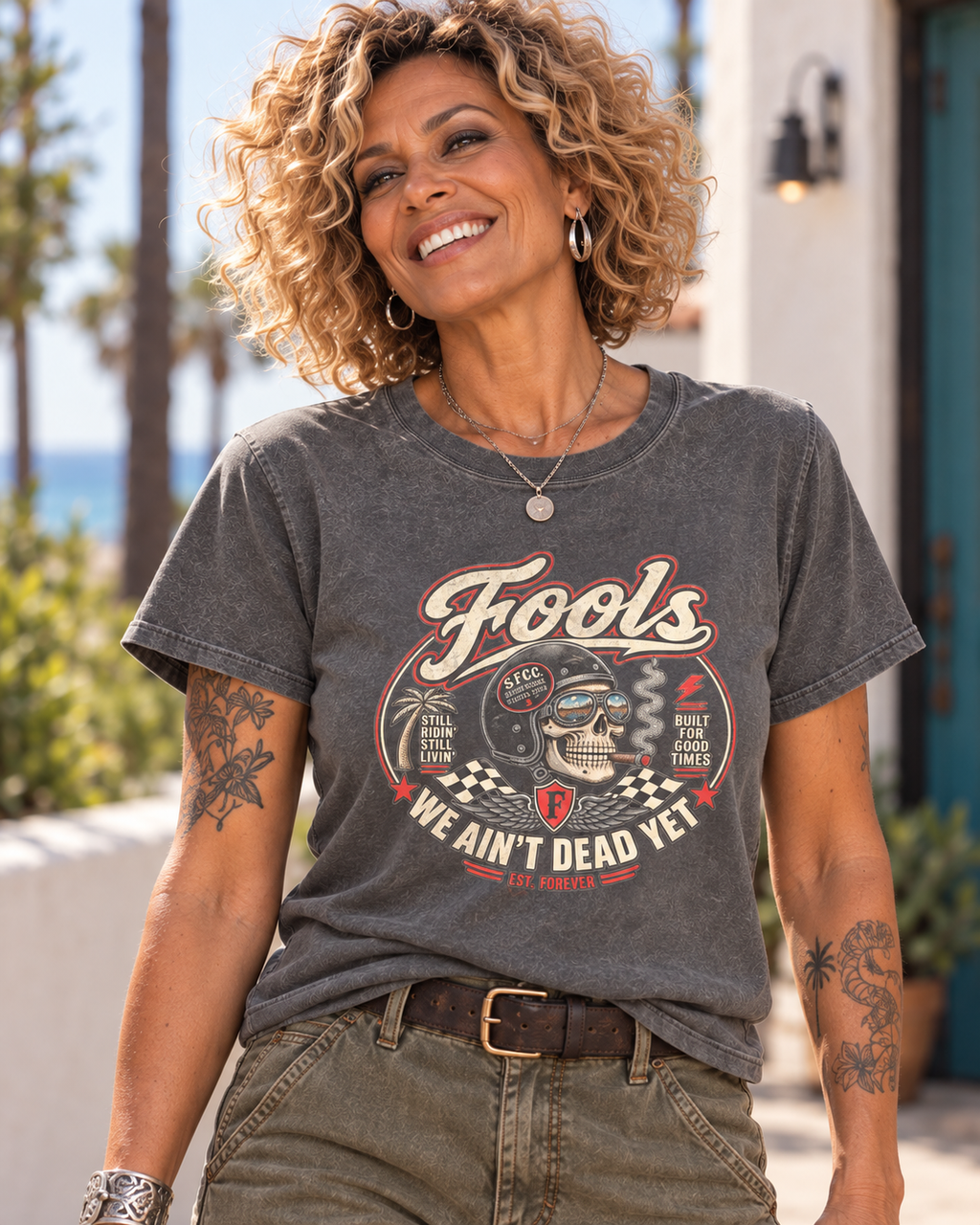 Close-up of the FOOLS Women's Faded We Ain't Dead Yet Tee in faded coal, showing the chest graphic with the curly-haired model and olive utility pants