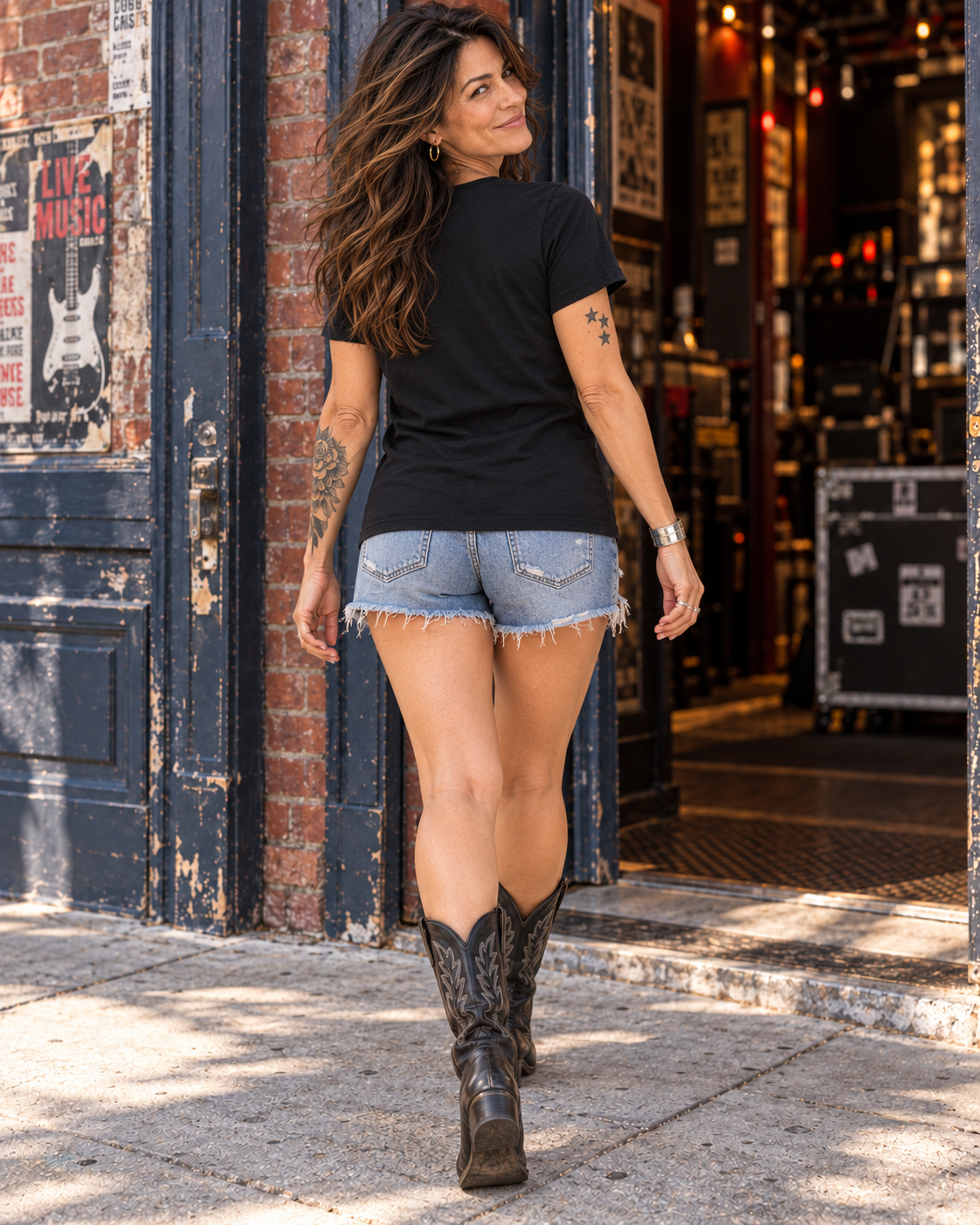 Back view of the FOOLS Women's We Ain't Dead Yet V-neck Tee in black, showing the plain back and untucked hem with denim shorts and black cowboy boots