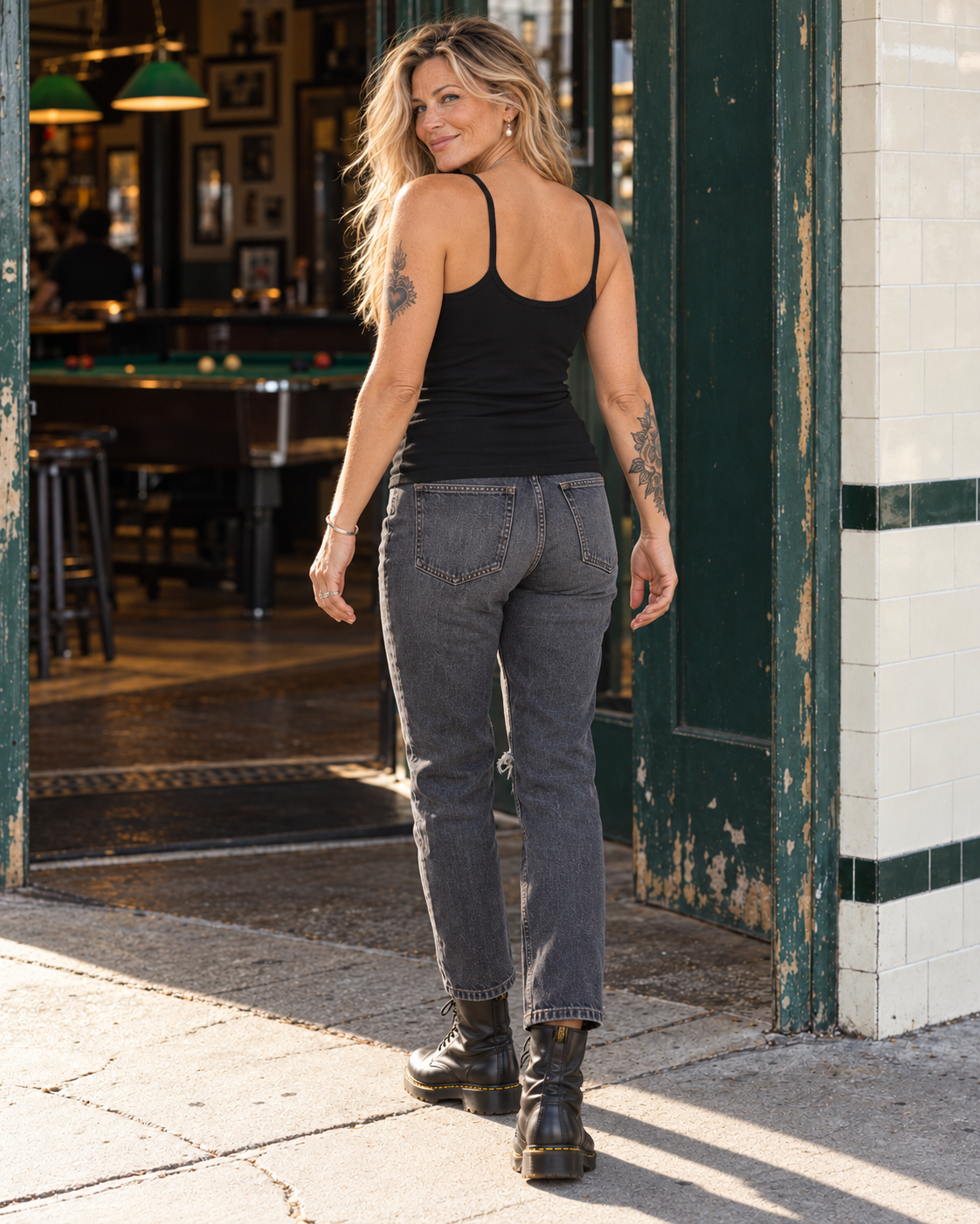 Back view of the FOOLS Women's Fitted Tank Top in black, showing the thin shoulder straps, low scoop back and untucked hem with charcoal jeans and black boots
