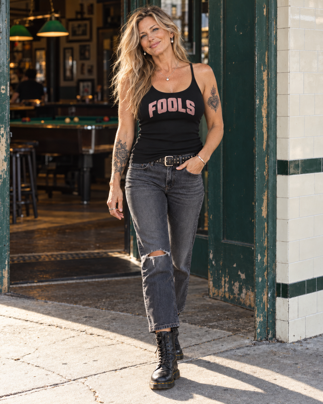 FOOLS Women's Fitted Tank Top in black with thin shoulder straps and pink varsity lettering, styled with charcoal jeans, black lace-up boots and pearl earrings