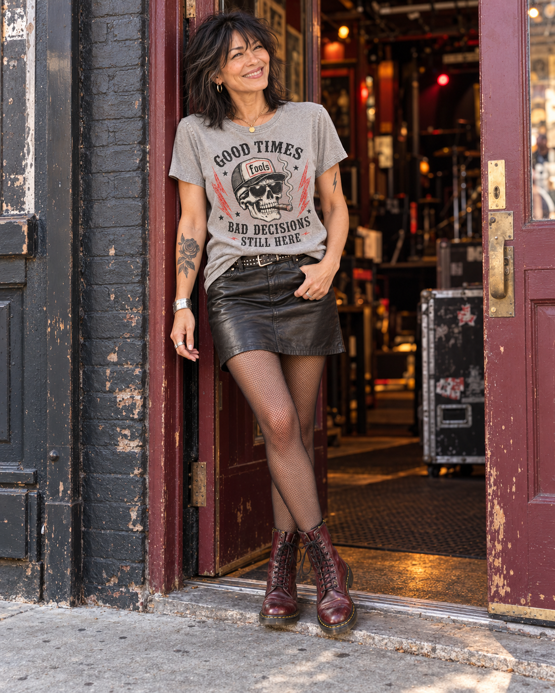 FOOLS Women's Still Here Faded Tee in faded stone, styled with a black leather skirt, fine fishnet tights and oxblood lace-up boots outside a music venue